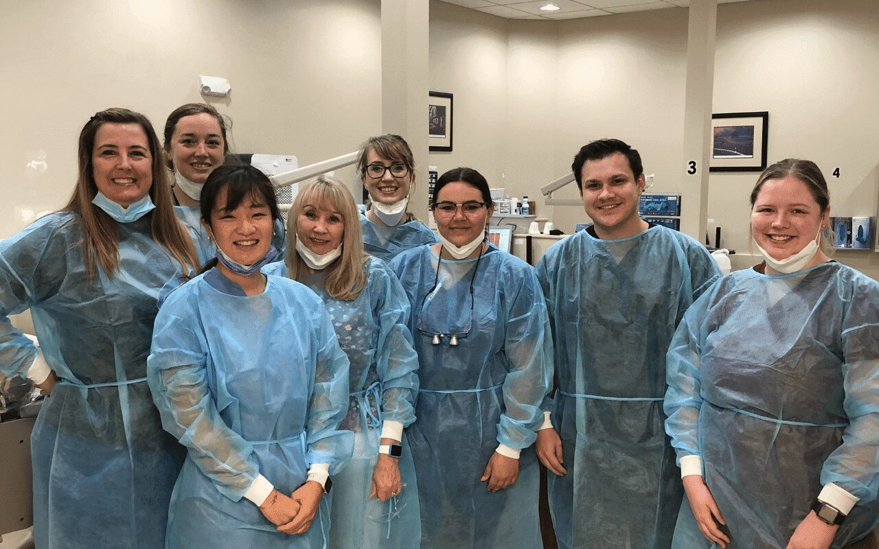 Group of six dental professionals wearing blue scrubs and masks in a clinic.